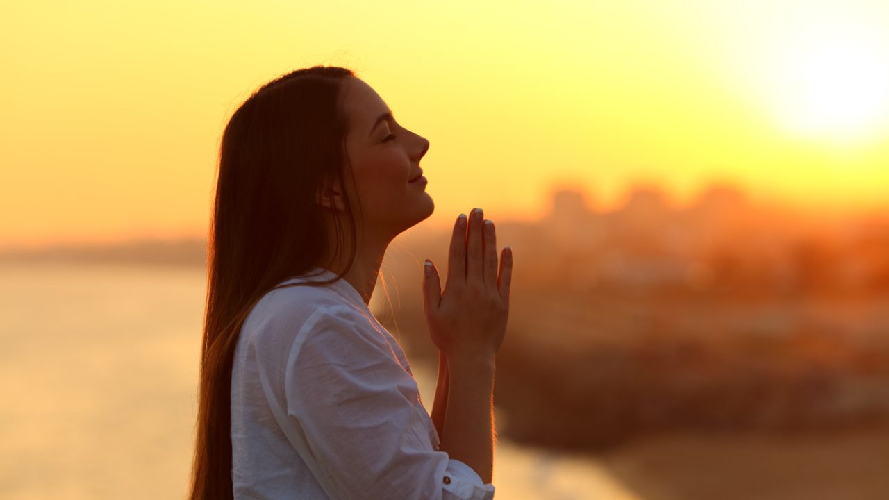 Mulher em oração ao pôr do sol
